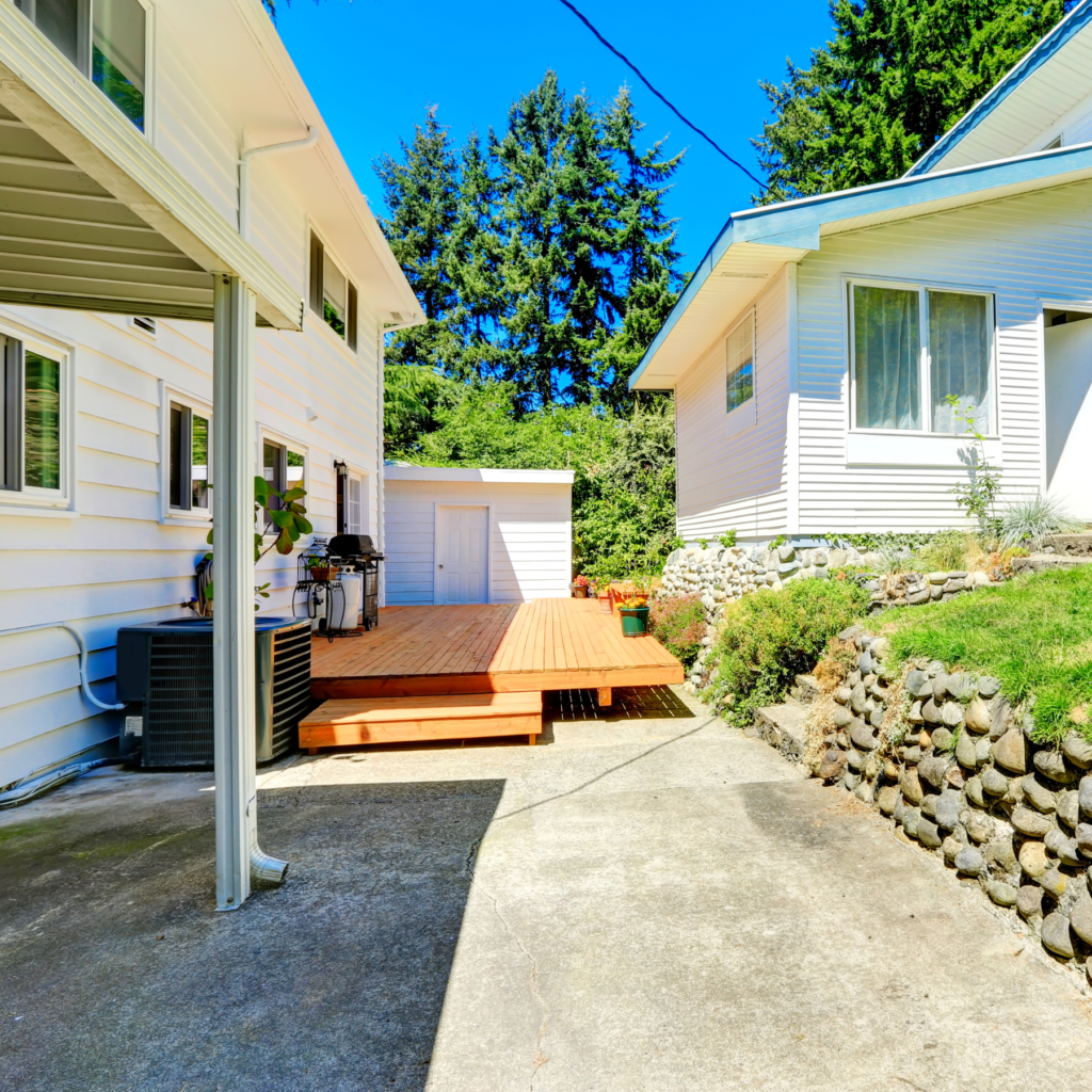 A pair of charming white houses with a porch deck and green lawn.