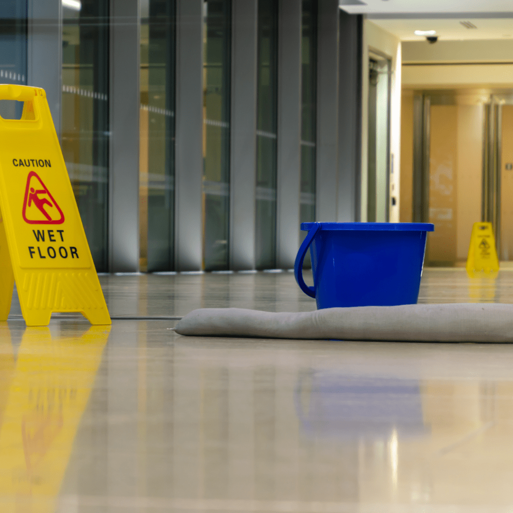 Yellow wet floor sign next to a blue maintenance bucket in a common area, indicating ongoing facility maintenance.