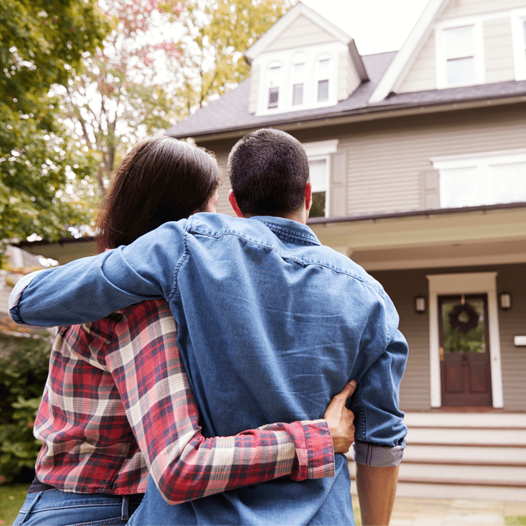 A couple looks at a two story house while holding each other in a hugged embrace