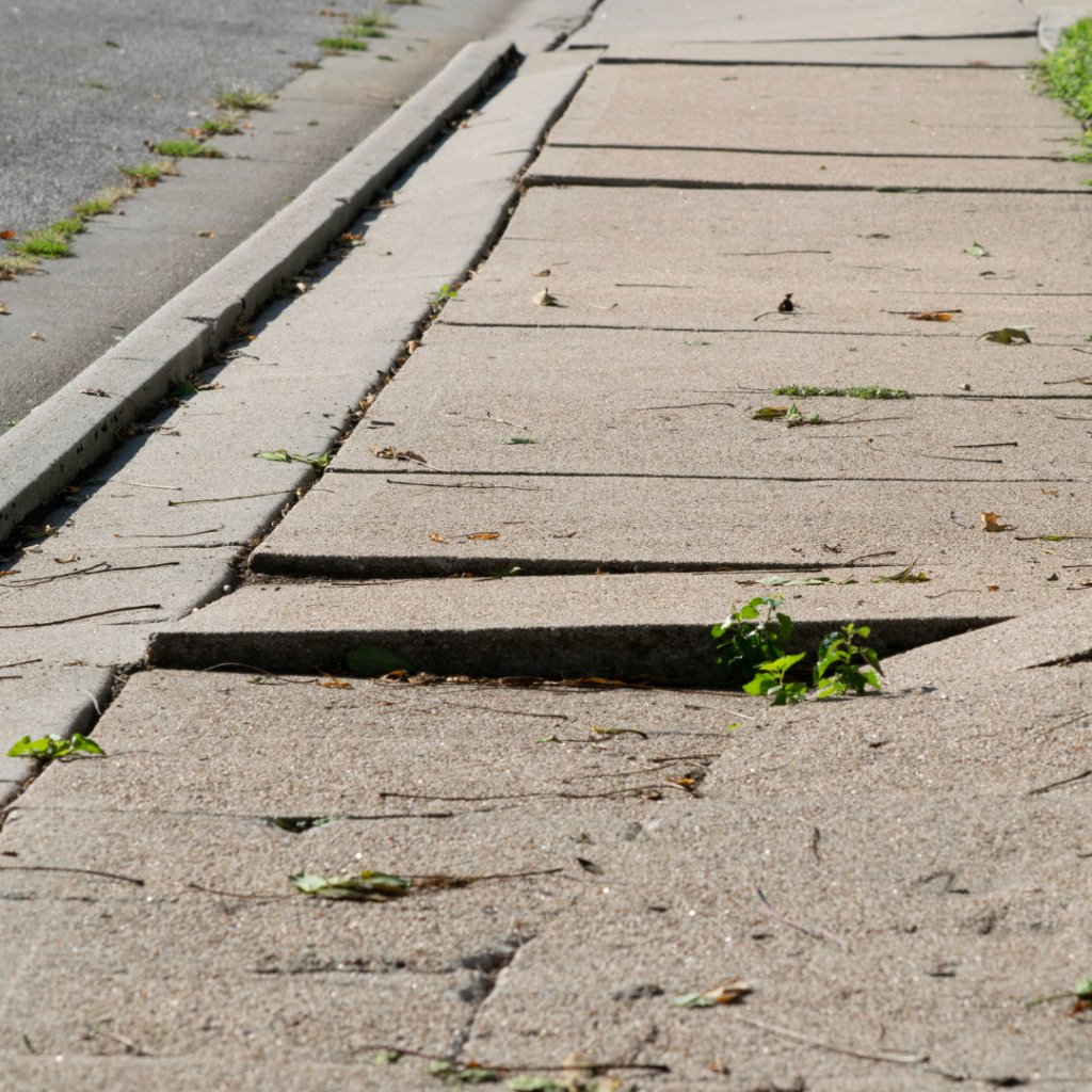 Uneven and cracked concrete sidewalk posing a safety hazard, requiring homeowner's attention for repair.